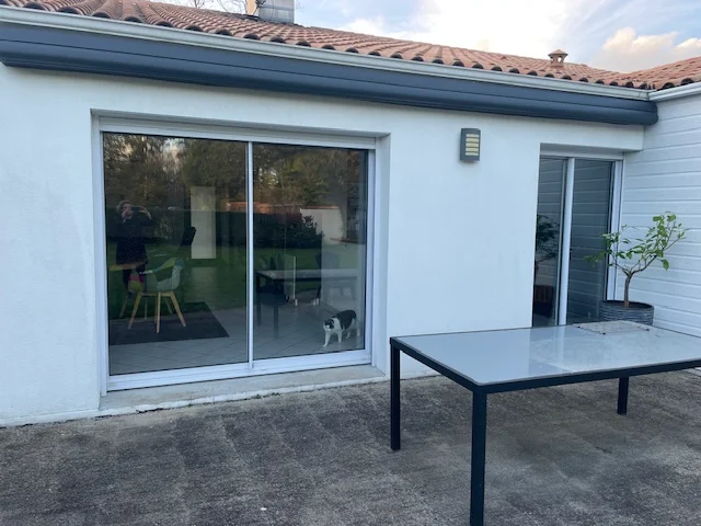 Photo d'une baie coulissante à deux vantaux blanche, et d'un porte fenêtre blanche. Deux menuiseries vétustes avant remplacement