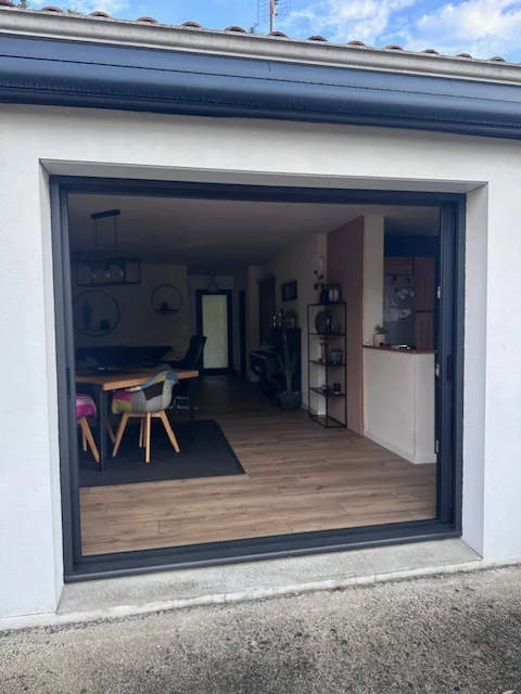 Baie coulissante ouverte sur un intérieur moderne, illustrant les menuiseries modernes en Vendée par Actiba Menuiseries.