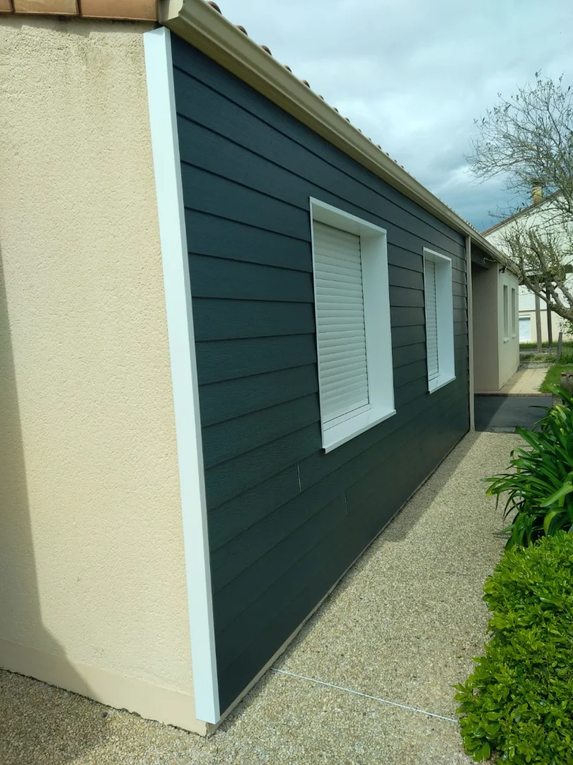 Bardage extérieur terminé. Un rendu sobre et moderne anthracite d'une maison qui fait ressortir les ouvertures et les volets blancs.