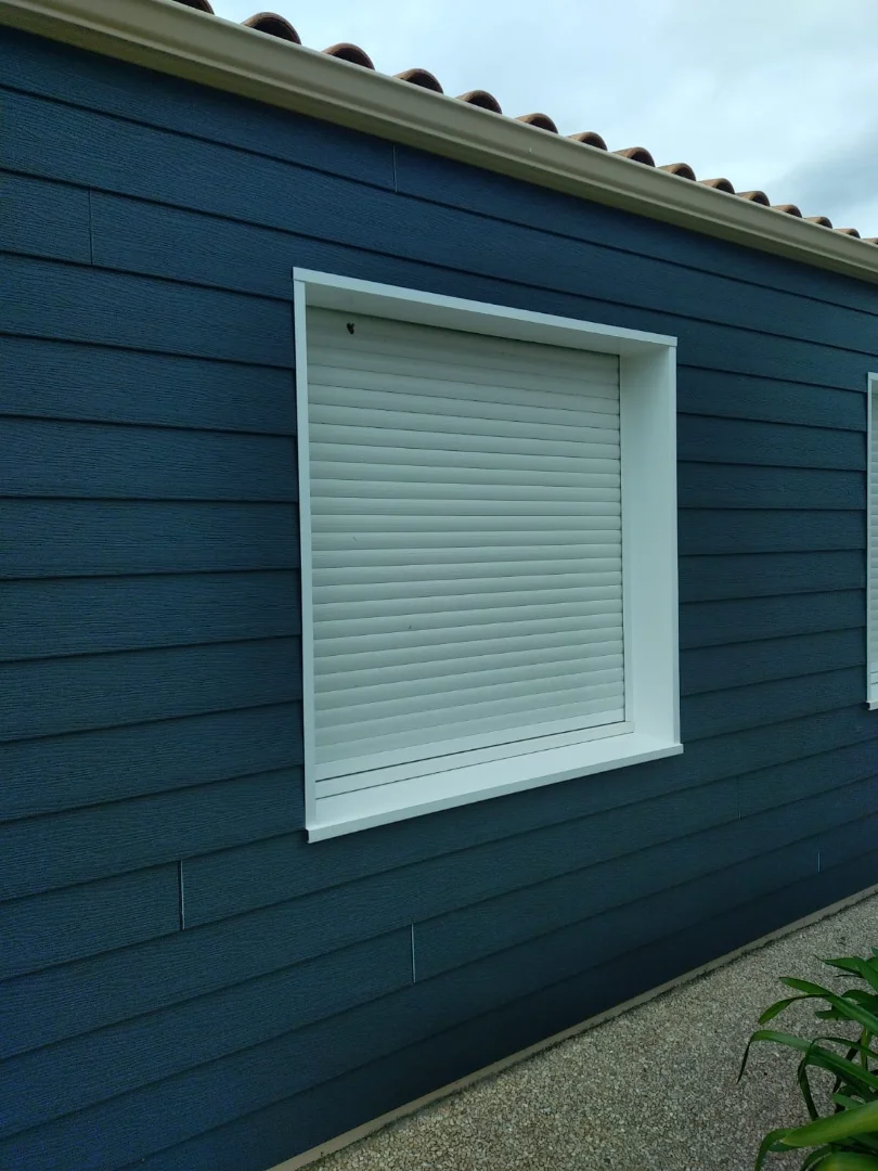 Bardage extérieur anthracite terminé offrant un rendu moderne et élégant, mettant en valeur les ouvertures et volets blancs de la maison.