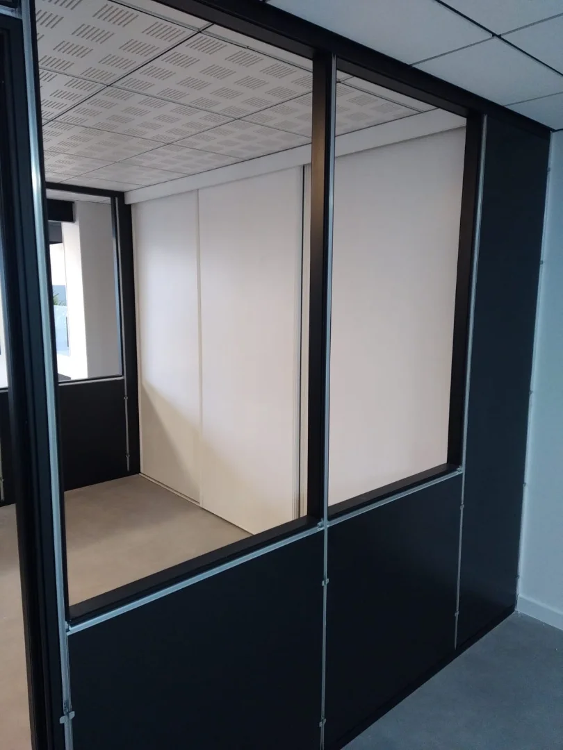 Bureau individuel séparé sur les deux côtés par des cloisons modulaires semi vitrées avec un grand placard dans le fond.