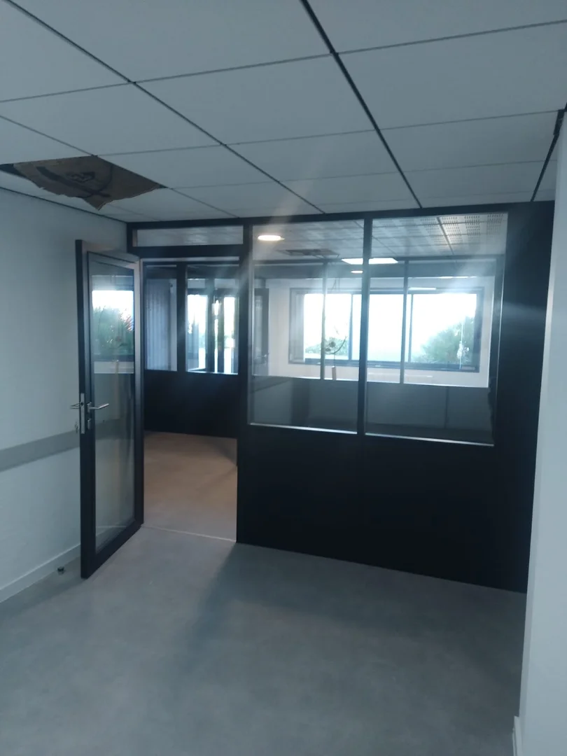 Bureau individuel avec un mur en cloison modulaire semi vitrée avec porte vitrée toute hauteur. Le bureau offre une grande luminosité.