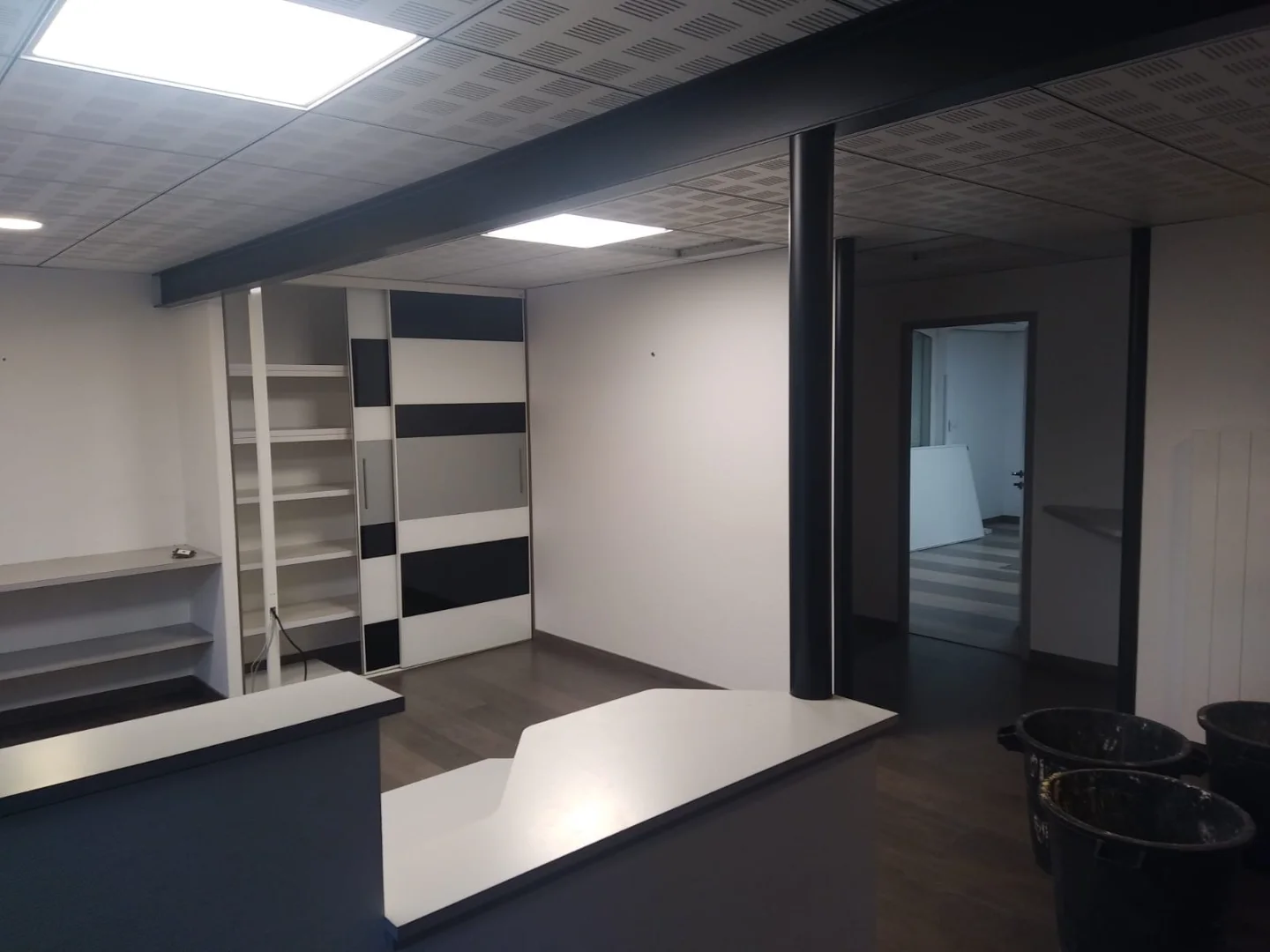 Grand bureau moderne noir et blanc présentant beaucoup de rangement grâce a des placards et des étagères.