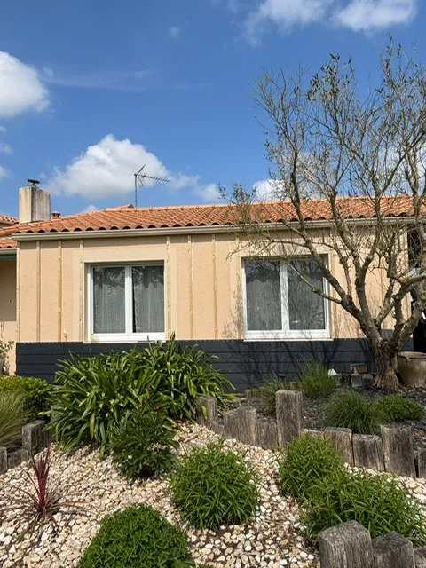 Maison vue de face, le bardage est en cours de réalisation, environ à 50% de la hauteur du mur. On aperçoit l'ossature en bois.