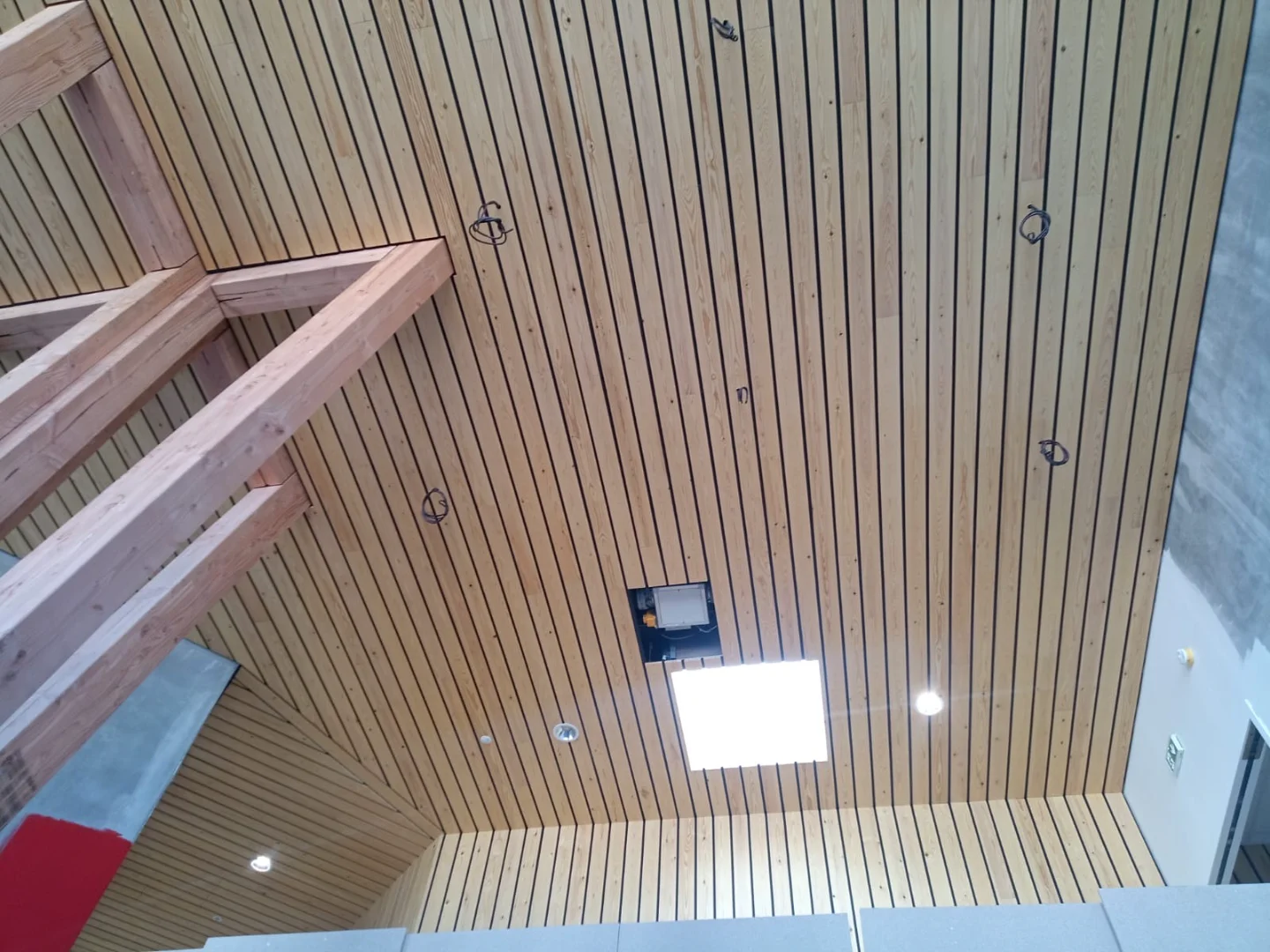 Revêtement intérieur en plafond claire-voie bois clair, combinant esthétique et fonctionnalité dans une pièce très haute.