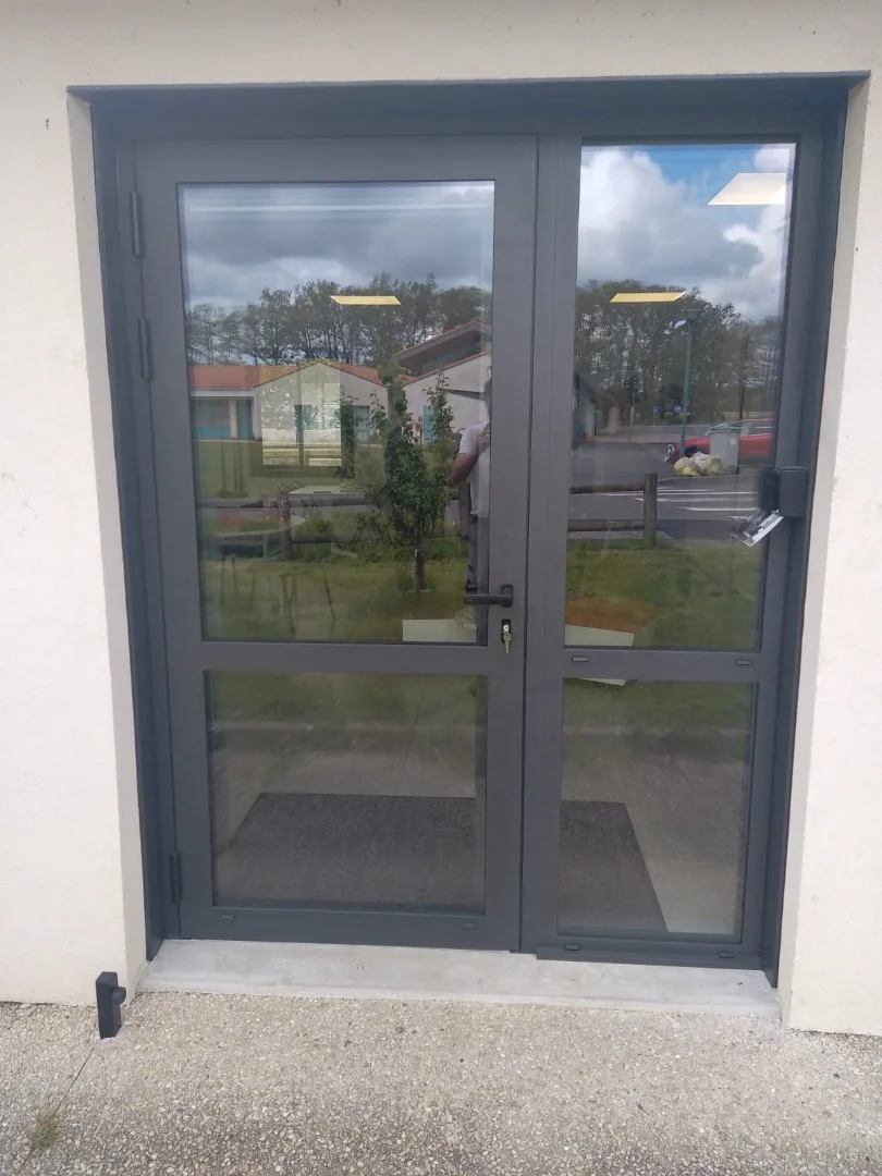 Point de vue extérieur du remplacement d'une porte vitrée anthracite d'une salle polyvalente.