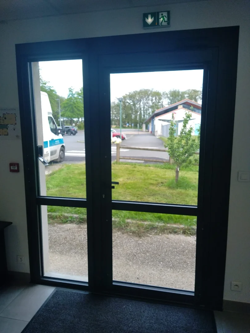 Porte d'entrée moderne d'une résidence urbaine, en verre et métal anthracite. Une porte sécurisée et fonctionnelle.
